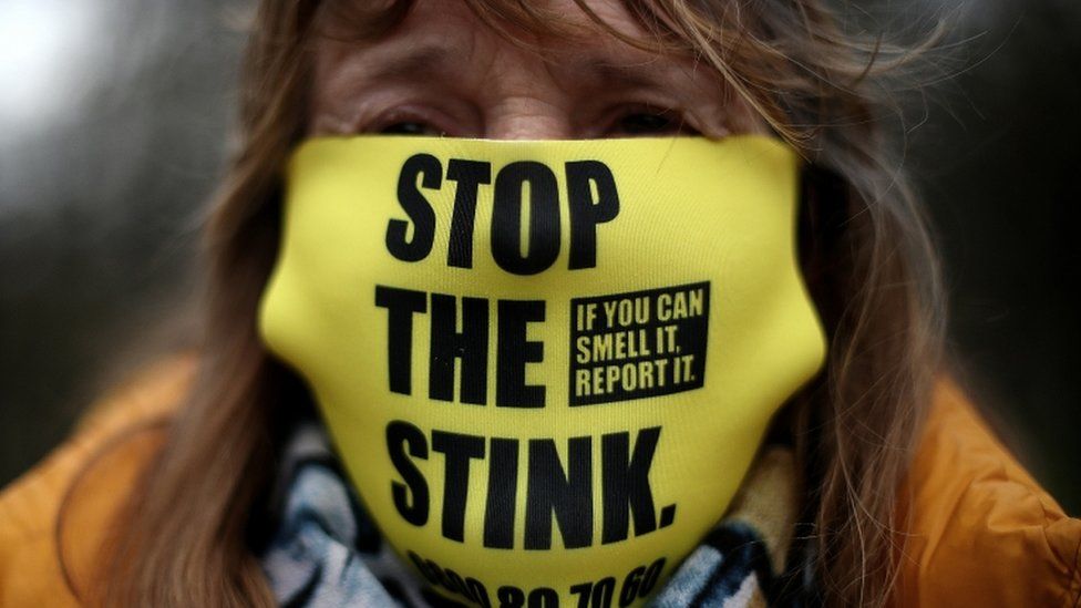 A woman wears a "Stop the Stink" face mask during a protest outside the gates of Walleys Quarry landfill in Silverdale