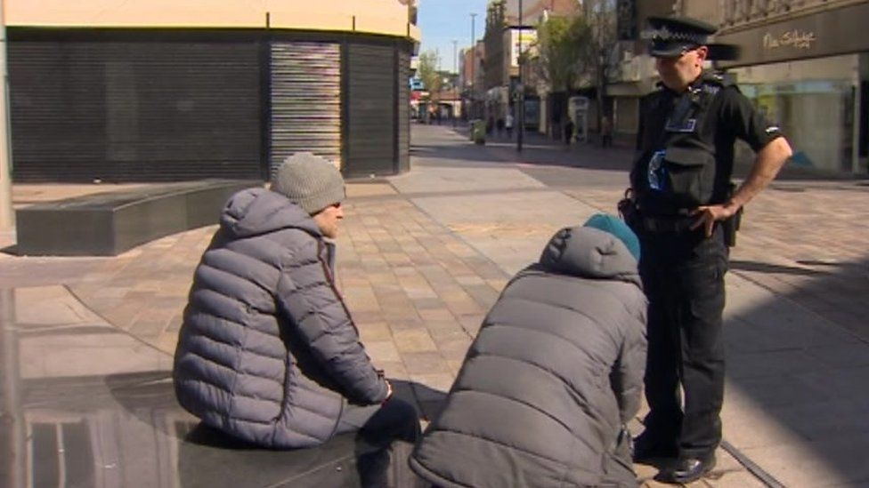 A Cleveland Police officer speaks to two men sat together on a bench