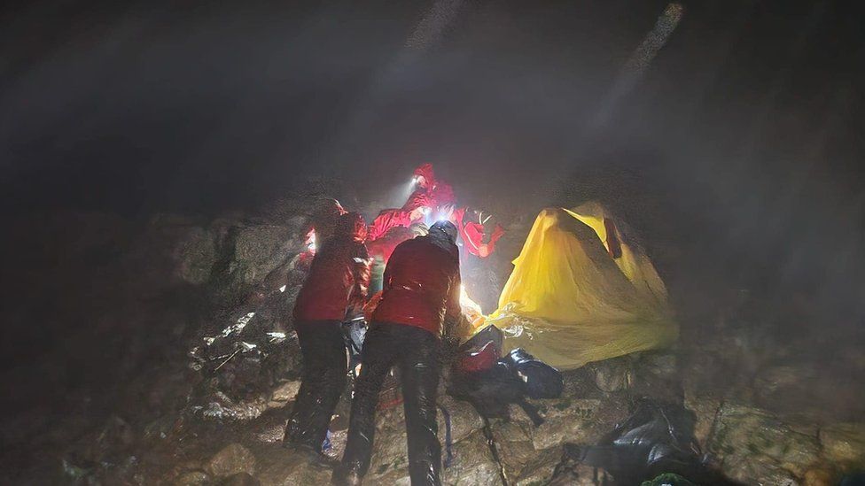 People in red coats have set up a yellow tent in the dark in heavy rain
