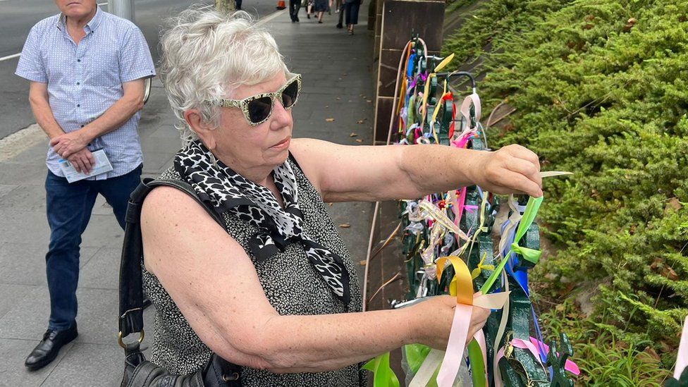 Maureen tying a ribbon to the fence