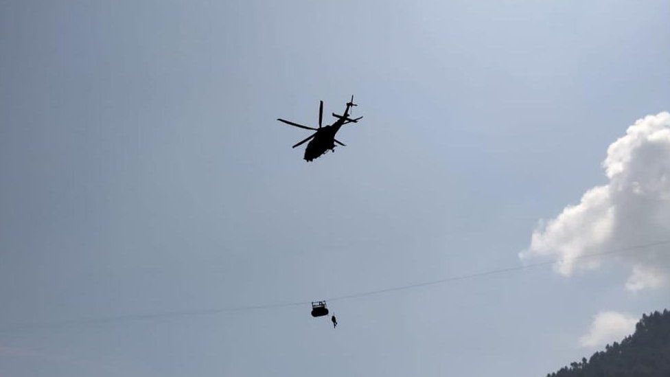 Army soldier slings down from a helicopter during a rescue mission to recover students stuck in a chairlift in Pashto village of mountainous Khyber Pakhtunkhwa province, on August 22, 2023