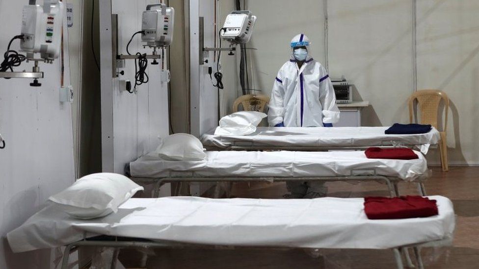 A woman wearing a protective suit stands next to beds inside a hospital that has been constructed to treat patients who test positive for the coronavirus disease (COVID-19),