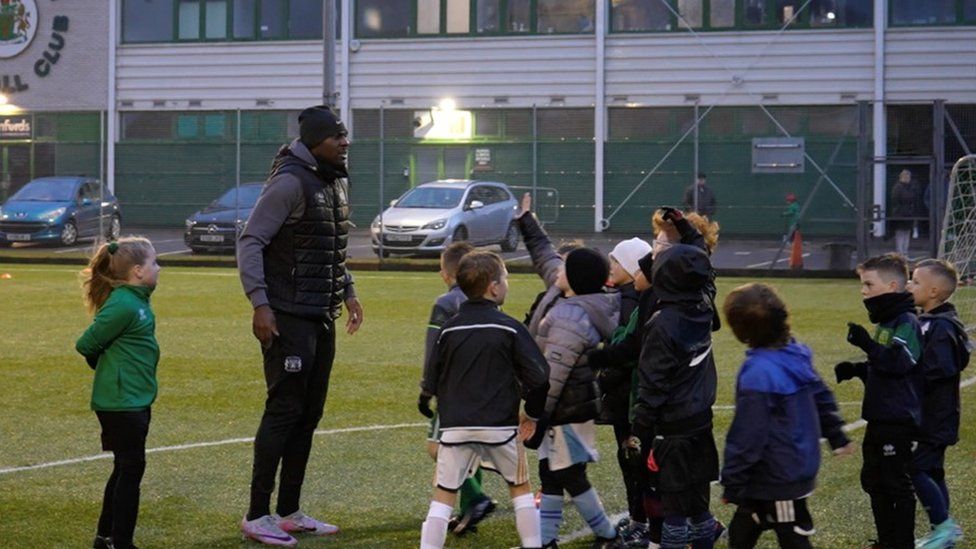 Man chats to group of children on football pitch