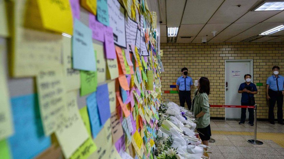 A mound of public tributes in the form of post-it messages and flowers outside the subway bathroom crime scene