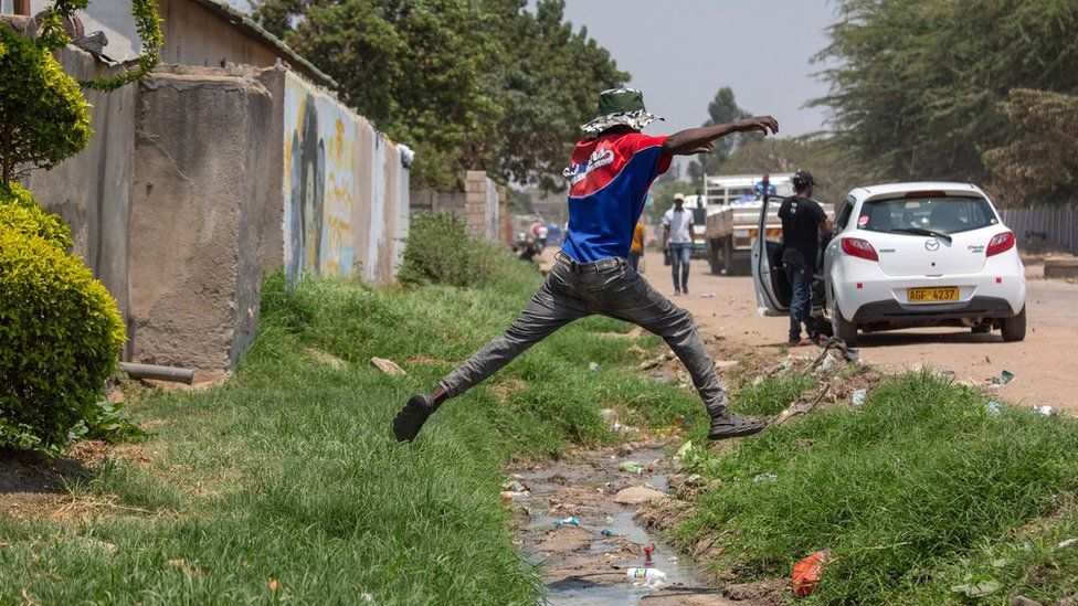 A man jumps over a storm water drain with flowing sewage in Chitungwiza, Zimbabwe, 09 October 2023.