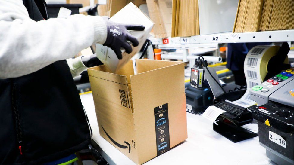 An Amazon worker wearing gloves, packing items into a box