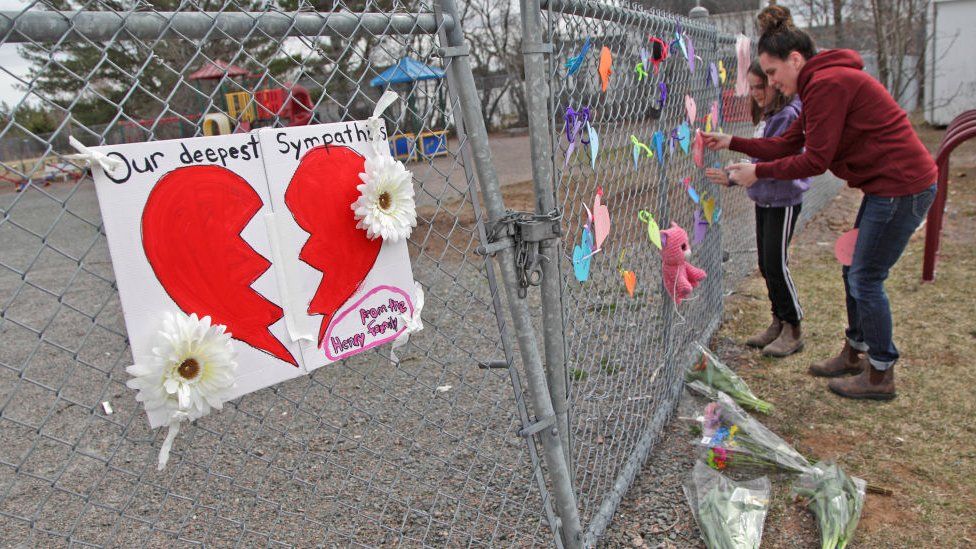 Женщина и ее дочь кладут сердце на забор растущего мемориала перед школой Деберта 20 апреля 2020 года в Деберте, Новая Шотландия, Канада