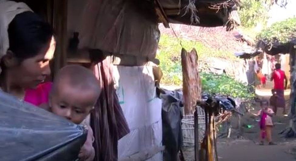 A woman holding a baby looks at another child in her village