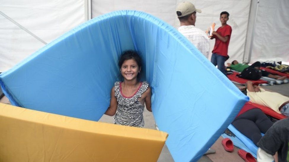 A girl smiles as she carries a mattrass in a stadium-turned-shelter in Mexico City