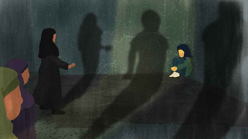 Three women approach a frightened girl, who is sitting in a ball in the corner of a dark room. Their shadows appear menacing.