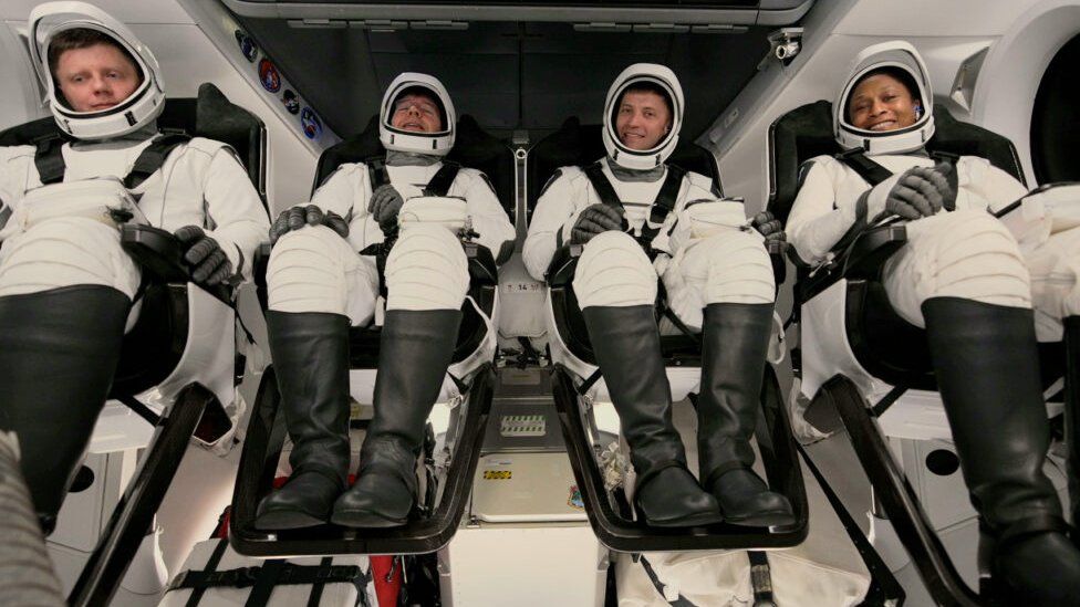 Four astronauts strapped to their seats in a capsule ready to go to space