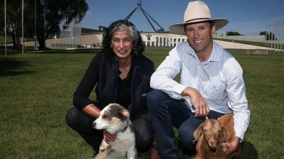 A man and a woman outside Australian parliament with a dog and a mini goat