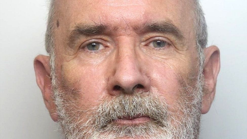 Timothy Darch looking at the camera for his custody mugshot, He has white hair and a white beard