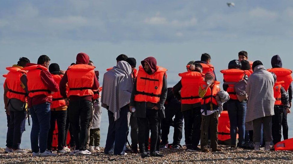 Группа людей, считавшихся мигрантами, на пляже в Дандженессе, Кент, после того, как RNLI спасла их в Ла-Манше после инцидента с небольшой лодкой