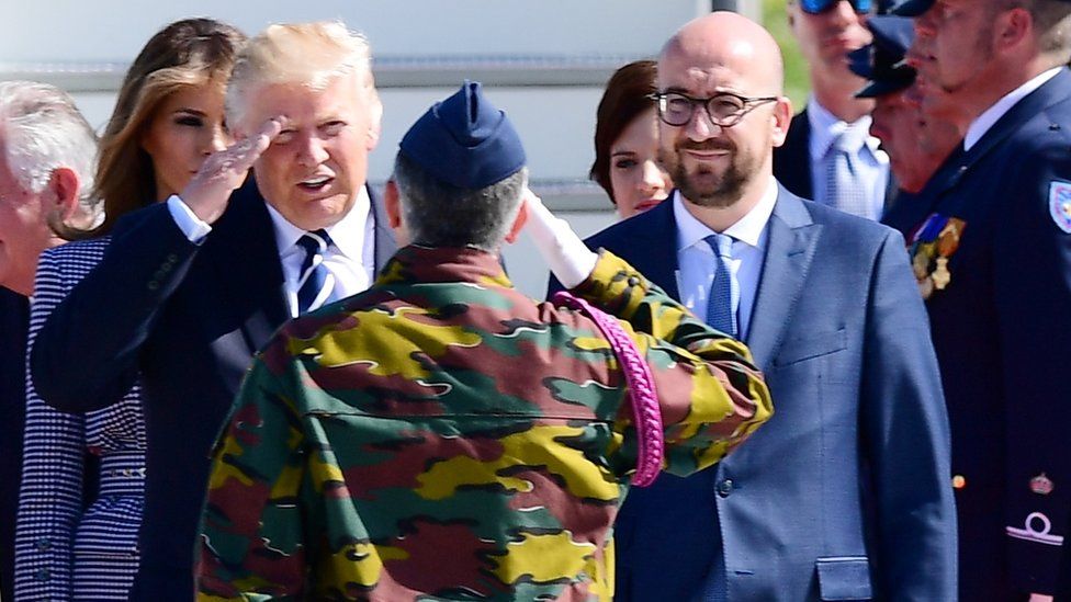 US President Donald Trump (L) and Belgian Prime Minister Charles Michel (R) stand in front of a military serviceman upon arrival at the Melsbroek military airport in Steenokkerzeel on May 24, 2017