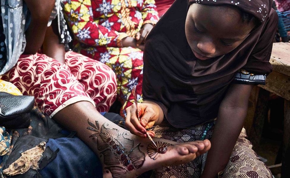 A girl painting henna on to a woman's foot in Bamako, Mali - Monday 20 August 2018