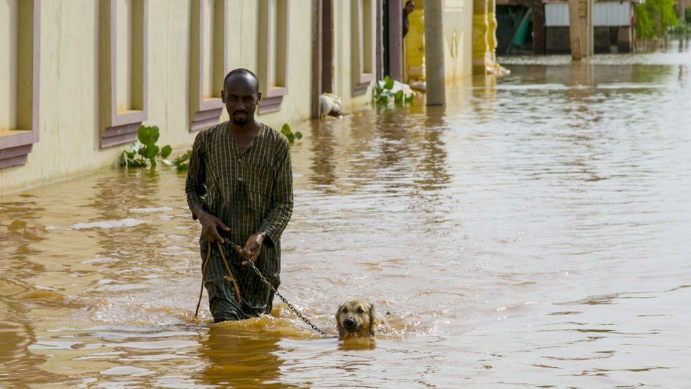 A Sudanese man wades through the floodwaters with his dog at Umm Dawm district in Khartoum, Sudan on September 8, 2020.