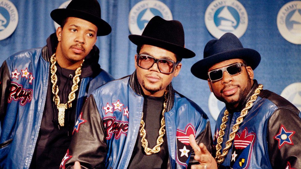 3/2/1988- RUN-DMC poses in full regalia that they popularized- heavy gold chains, hats, sunglasses, and Adidas track suits. They have just received the Grammy Awards