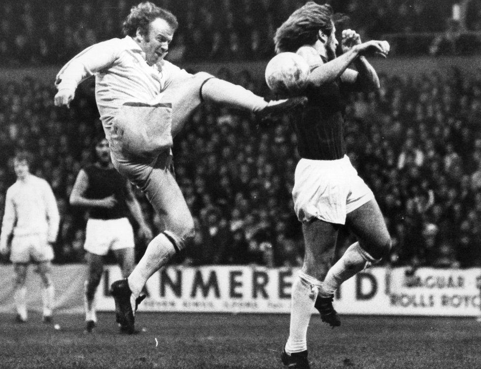 Billy Bremner leaps high to kick the ball as West Ham United's Graham Paddon attempts a block during a match in 1974