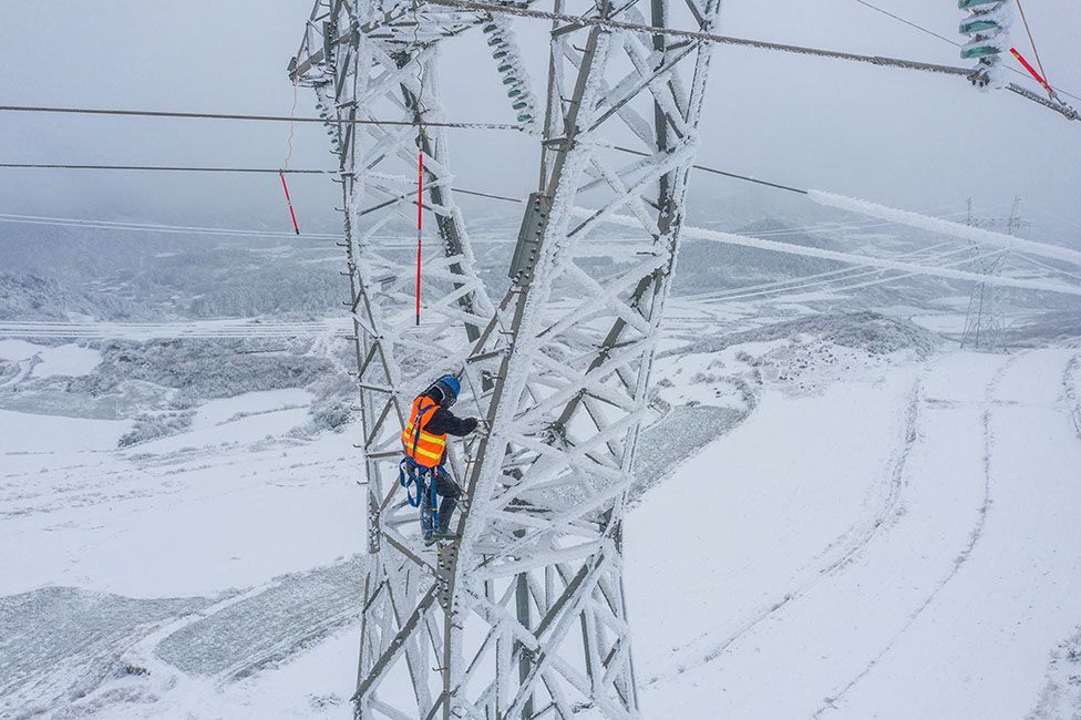 A worker climbs a pylon to remove ice from electric transmission lines as it snows in Bijie in China's southwestern Guizhou province on 21 February 2022