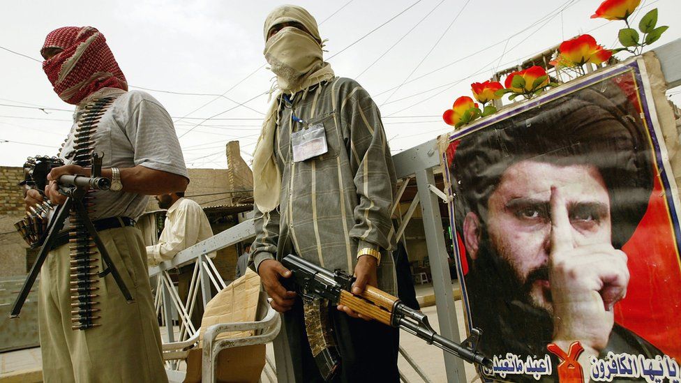 Mehdi Army fighters stand next to a poster of Moqtada Sadr at a checkpoint in Najaf, Iraq (30 April 2004)
