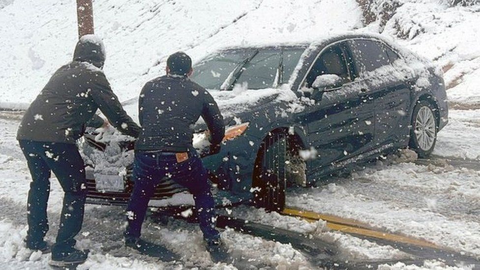 Two men try to stop a car from sliding down an icy roads during a snow storm in Rancho Cucamonga, California. Photo: 25 February 2023