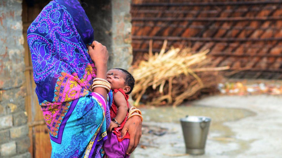 Индийская женщина стоит с ребенком возле своего дома в сельской Индии.