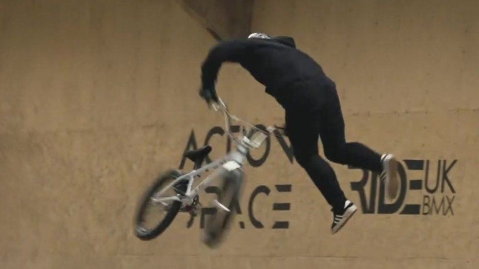 Kieran Reilly wearing a helmet and hanging onto his bike on a quarter pipe