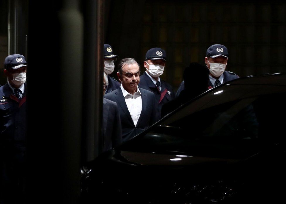 Former Nissan chairman Carlos Ghosn is escorted out of the Tokyo Detention House in April following his release on bail for multiple charges of financial misconduct.