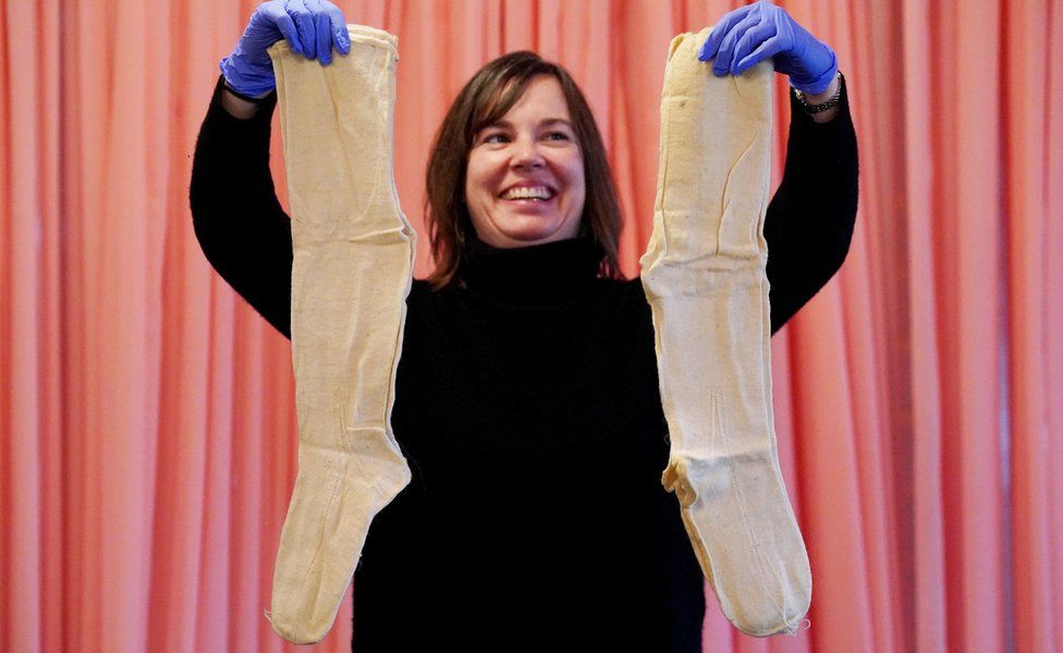 A pair of beige-coloured stockings being held up by a staff member at the National Archives