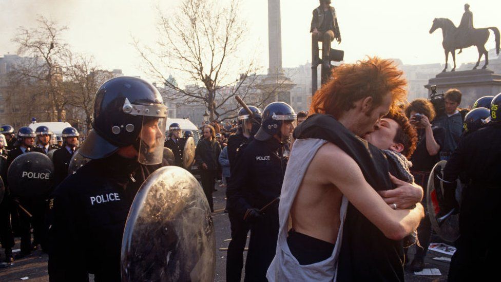 A couple kiss near police officers in the middle of the Poll Tax