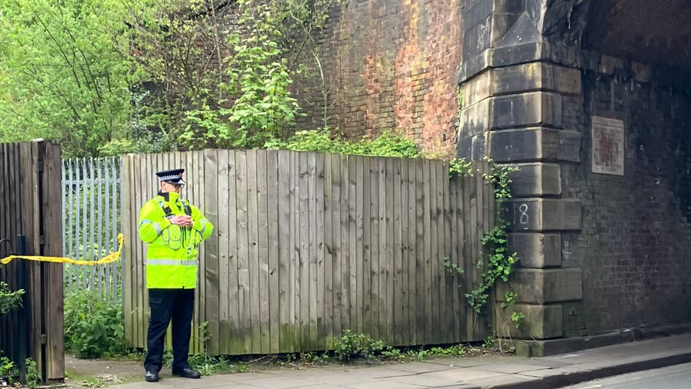 A police officer stands guard by the entrance to the railway line off Worsley Road
