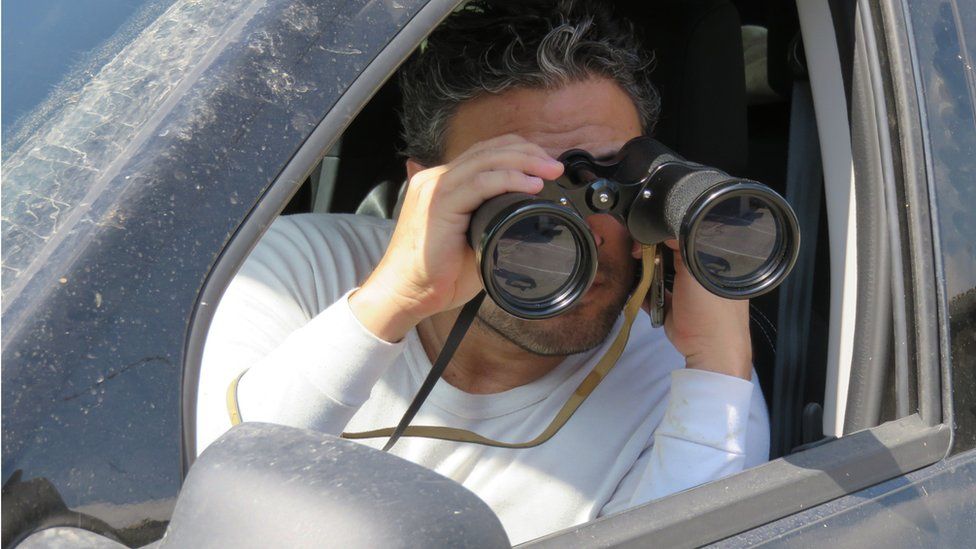 Man looks out of car holding binoculars