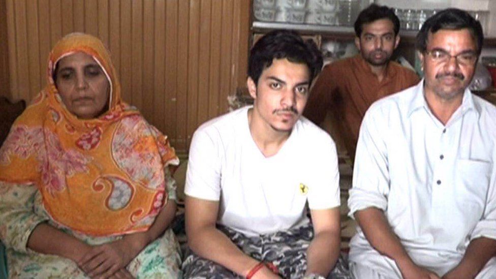 Picture of Hassan Khan sitting down looking straight at the camera with his parents on either side