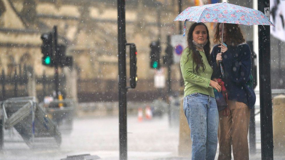 Two young women shelter under an umbrella in Parliament Square in central London amid heavy rain