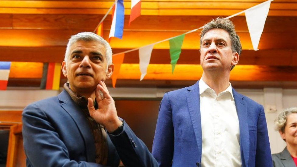 Sadiq Khan and Ed Miliband listening to someone as they visit a school in north London