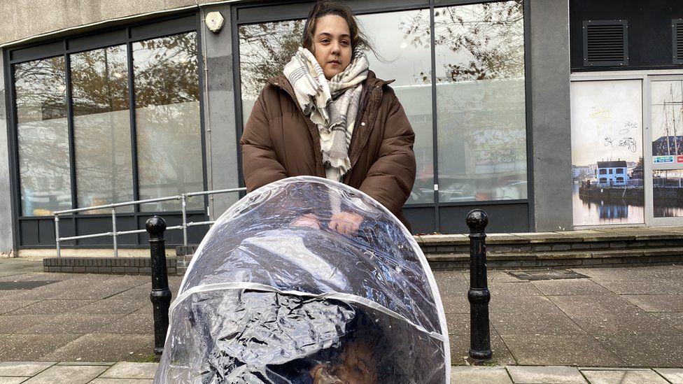Barton House resident Yasmin standing on the street outside of the Holiday Inn Hotel with a pram and warm clothes on