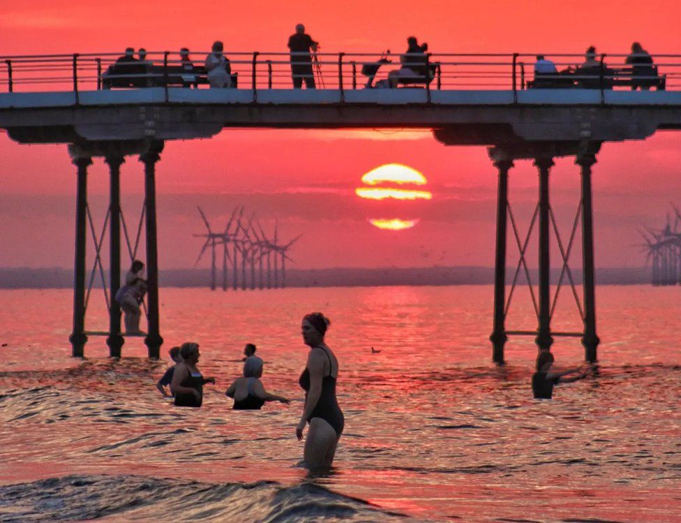 Several women wade in the sea next to a pier at Saltburn as the sunsets