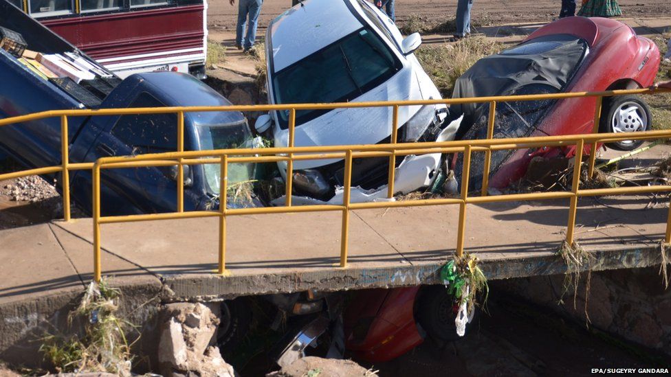 Three cars crused together on the side of a road after being swept away by floodwaters