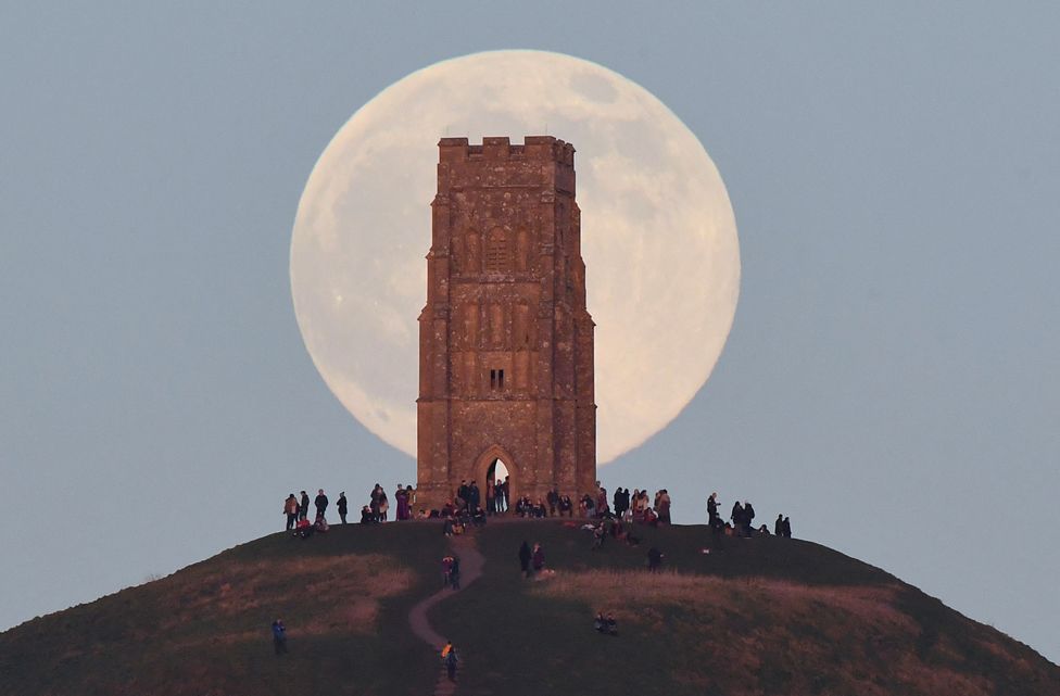 People stand beside St Michael's Tower as they watch the full moon rise behind Glastonbury Tor in Glastonbury, on 17 January 2022