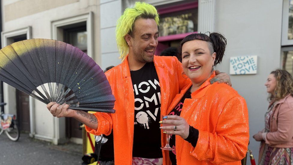 Connor Kerr holding a fan and Becky Bellamy - both wearing orange sequin jackets