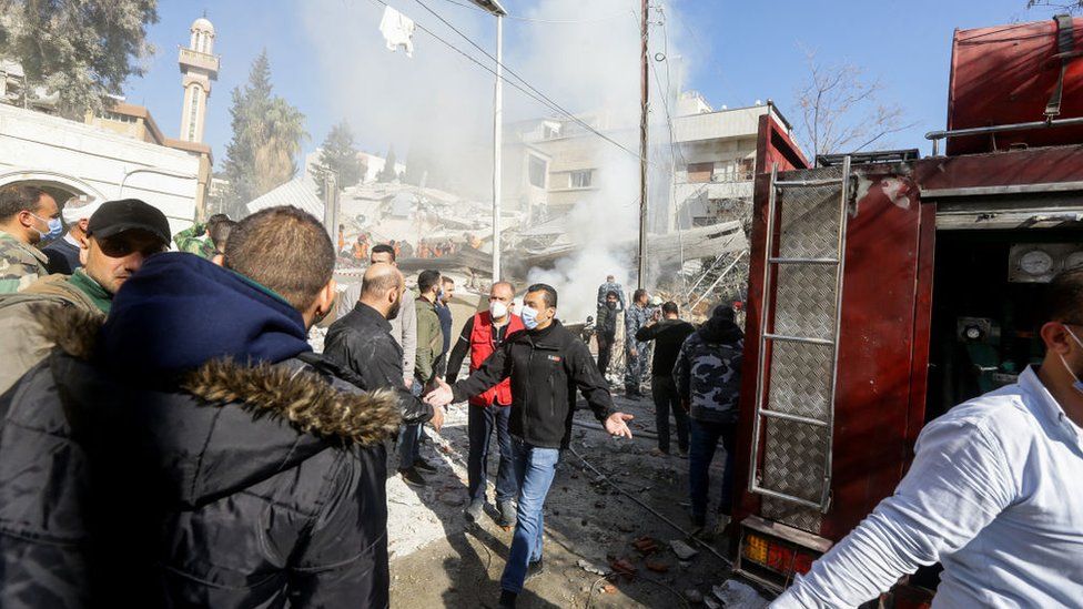 People next to a fire truck and destroyed building in Damascus