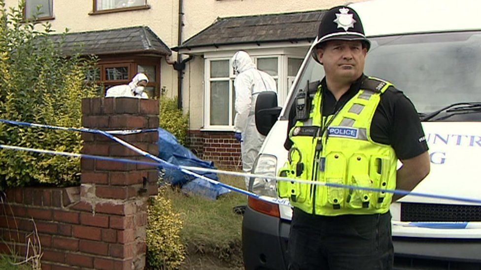 Police officer and forensics team outside a house