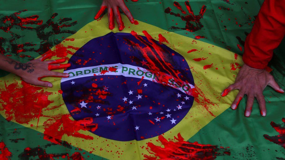 Black movement activists put their hands, covered by red paint, on a Brazilian flag, during a protest against racism and police violence in Sao Paulo
