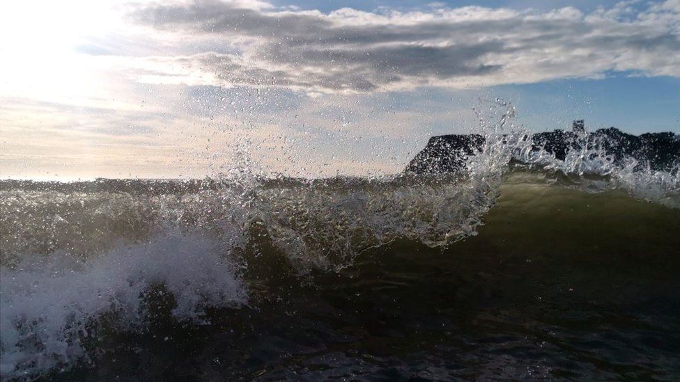 Pictured is a breaking wave with a headland in the background