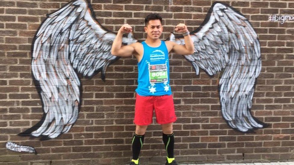 Neil Calucag standing in front of a pair of painted angel wings