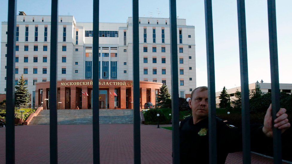A convoy guard stands behind a fence around the building of the Moscow Regional Court outside Moscow