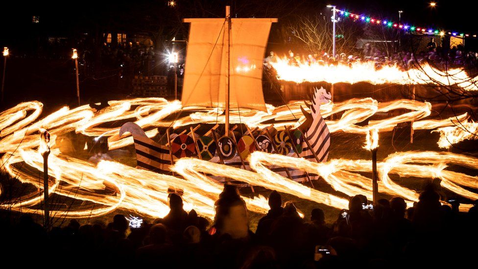 Fire-lit torches being swung around a Viking Longship
