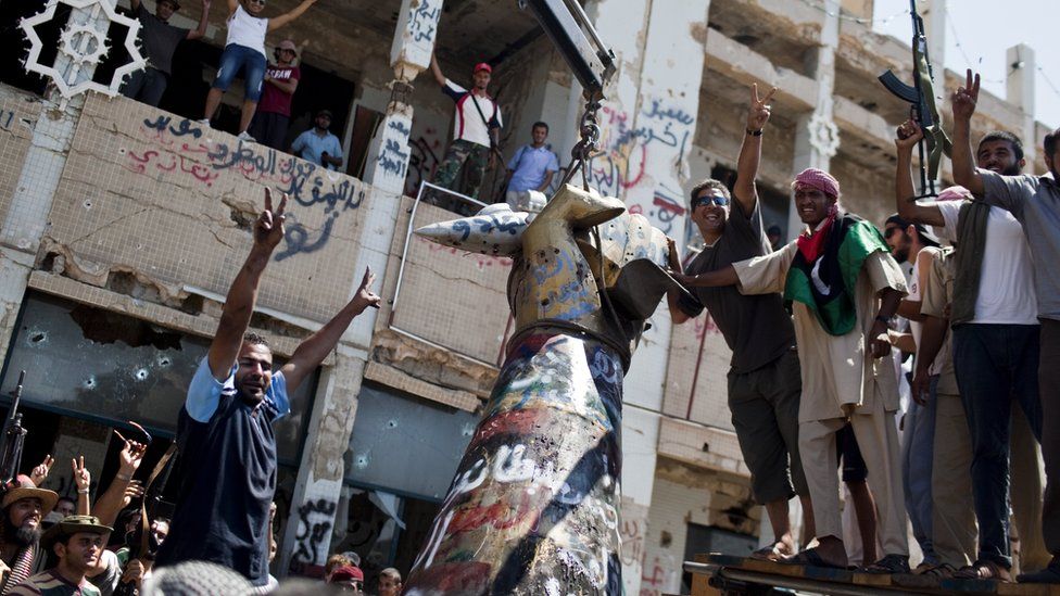 Rebels celebrate as they tear down 'hand crushing a plane' statue in Colonel Gaddafi's compound in Tripoli