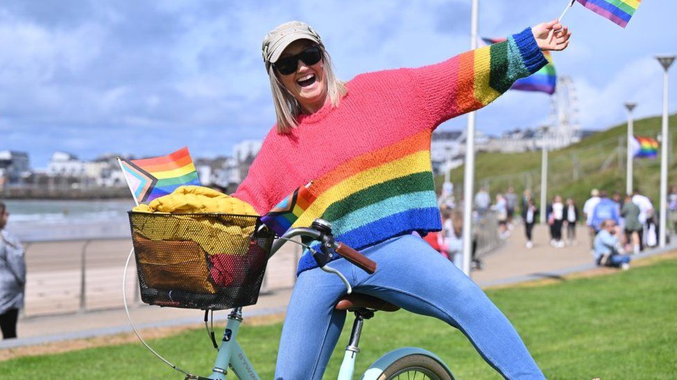 A woman holding Pride flags while riding a bike at the town's first Pride rally on Saturday.
